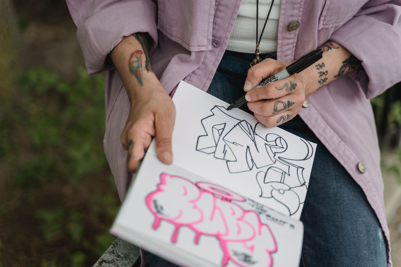 From above of crop unrecognizable artist with felt pen in left hand drawing in album in nature